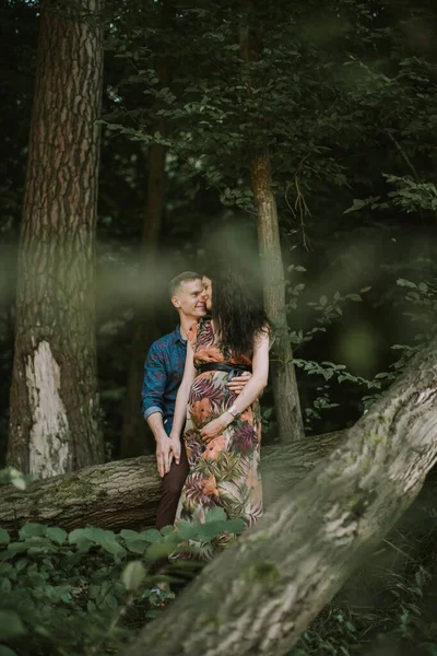 Boldog terhes pár, állva a gyönyörű nyári erdőben, ölelkezve és mosolyogva egymást — Stock Fotó