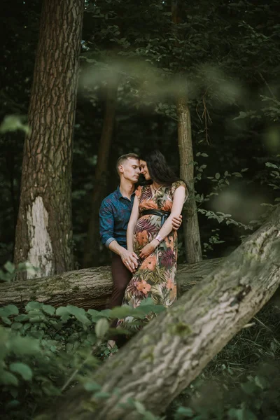 快乐的怀孕夫妇，站在美丽的夏日森林里，互相拥抱，互相微笑 — 图库照片