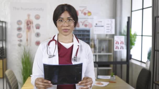 Afro american female doctor in uniform posing indoors, holding x-ray scan in hands — Stock Video