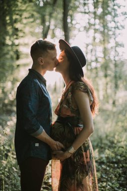 Yakışıklı adam ve güzel hamile karısı, ormandaki güzel günbatımının arka planında duruyorlar.