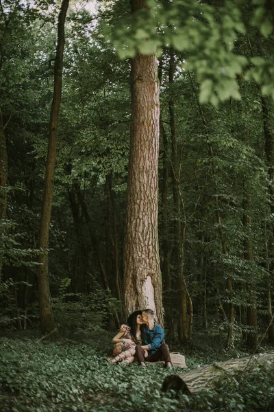 Мужчина и женщина, наслаждаясь прогулкой в лесу, сидя под большим деревом, обнимаясь и целуясь — стоковое фото