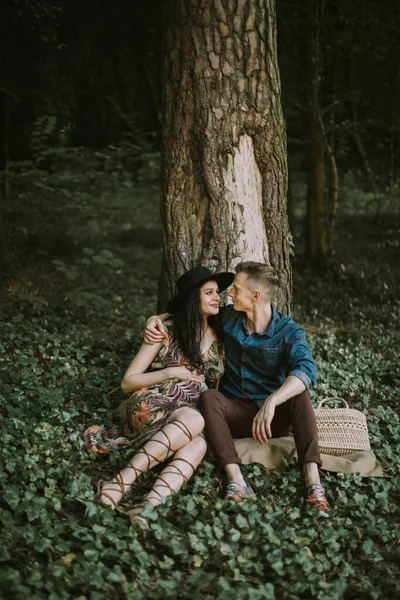 Schwangere und gutaussehender Mann sitzen unter dem Baum im Wald, umarmen sich und schauen einander an — Stockfoto