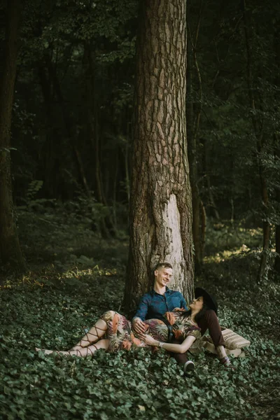 Jolie jeune femme enceinte allongée sur les jambes de son mari, assise sous l'arbre dans la forêt — Photo