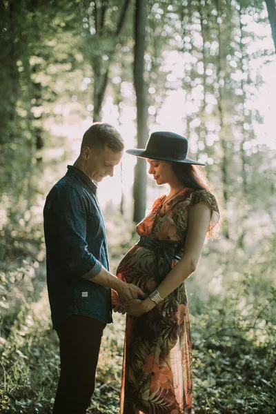 Homme et sa jolie femme enceinte, debout sur le fond de beau coucher de soleil dans la forêt d'été — Photo