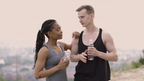 Likable πολυεθνική ζευγάρι σε αθλητικά ρούχα με μπουκάλι νερό σε εξωτερικούς χώρους — Αρχείο Βίντεο