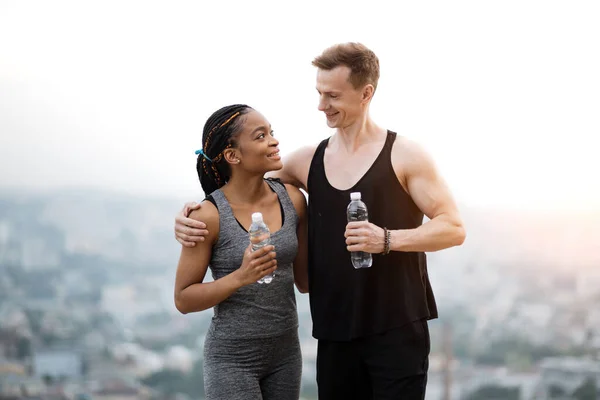 Casal positivo em sportswear com garrafa de água ao ar livre — Fotografia de Stock