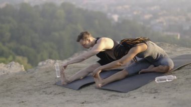 Aktif kıyafetli genç çift yoga minderinde bacaklarını esnetiyor.