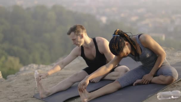 Молодая пара в активной одежде растягивает ноги на коврике для йоги — стоковое видео