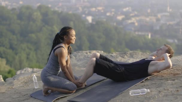 Muž dělá cvičení pro břicha, zatímco žena drží jeho nohy — Stock video