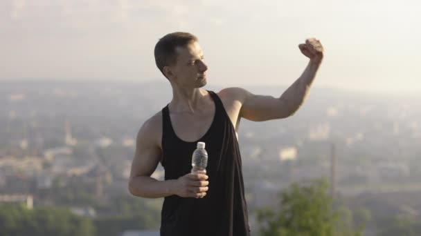 Atleta masculino demostrando sus bíceps musculares a la cámara, posando al aire libre — Vídeo de stock