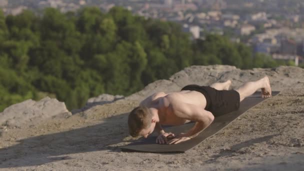 Sportlicher Mann macht Liegestütze im Freien an einem sonnigen Morgen auf einem hohen Hügel mit atemberaubendem Blick auf die Stadt. — Stockvideo