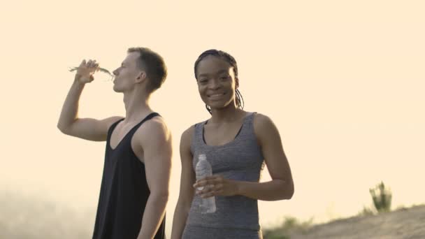 Багатоетнічна пара в спортивному одязі питна вода на відкритому повітрі — стокове відео