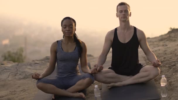 Multi-etnische paar mediteren op yoga mat buiten — Stockvideo