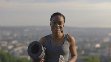 Aktif kıyafetli Afrikalı kadın elinde bir şişe su tutuyor.