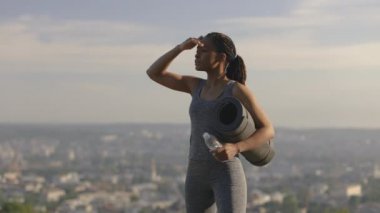 Elinde yoga minderi ve su şişesi tutan siyahi kadın.