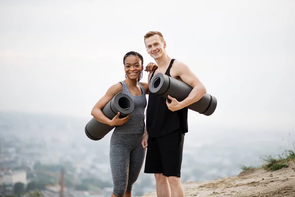 Casal multicultural em roupas esportivas segurando tapete de ioga — Fotografia de Stock