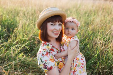 Güzel gülümseyen genç bir anne kucağında küçük bir kız çocuğu, sarılıyor ve kameraya poz veriyor.