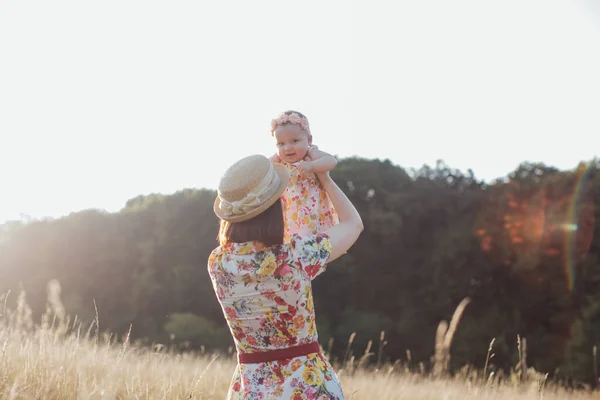 Anne kollarında dönüyor. Küçük mutlu bir kız çocuğu. Yaz tarlasında, gün batımının ışınlarında. — Stok fotoğraf