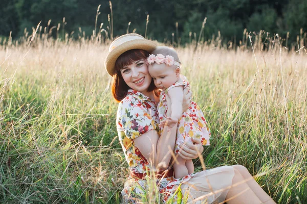 夏の日の畑で可愛い娘と一緒に草の上に座っている若い美しい女性 — ストック写真