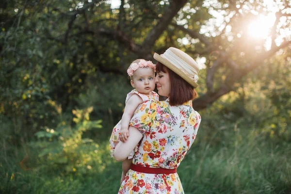 Вид ззаду красива мати тримає дитину на руках у саду. Маленька донька дивиться на камеру . — стокове фото