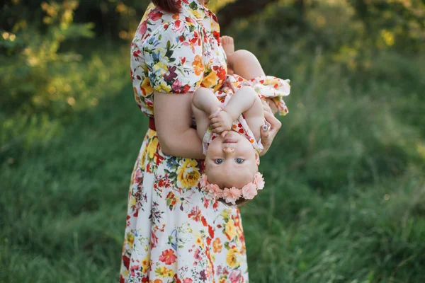 Elbiseli bebek ve kafasında turuncu çelenk. Annesinin elinde kameraya bakarken komik. — Stok fotoğraf