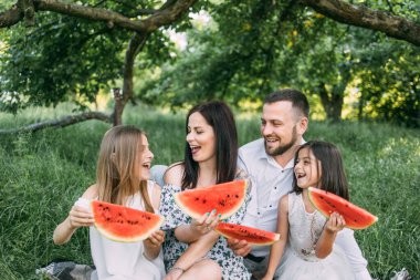 Bahçede ellerinde karpuzla oturan çocuklu bir çift.