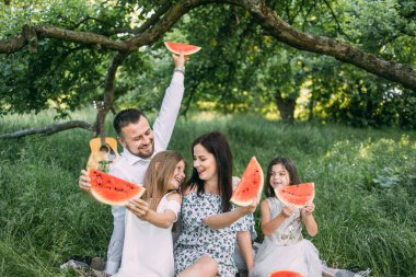 Piknikte karpuz yiyen iki çocuklu genç ebeveynler.