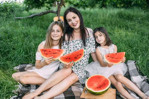 Woman with two daughters sweet watermelon on picnic