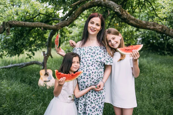 Pregnant woman with two kids eating watermelon outdoors