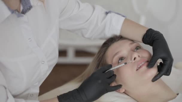 Lipvergroting en correctie formulier. Cosmetologische behandeling. Mooie jonge blonde vrouw die schoonheidsinjectie krijgt voor lippen. Close-up van de handen van de cosmetoloog die injectie in vrouwelijke lippen. — Stockvideo