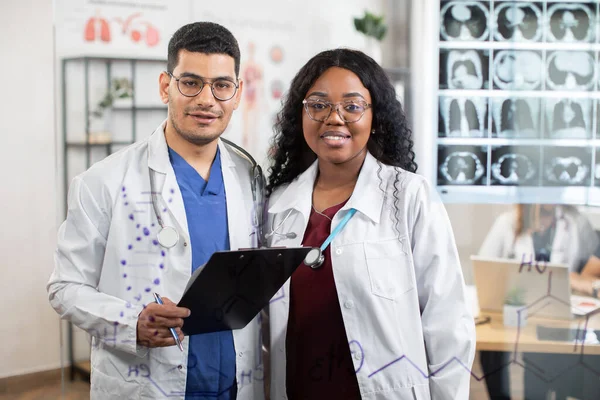 Multiraciala läkare, poserar framför kameran, står bakom den stora glasväggen med tomografi scan — Stockfoto