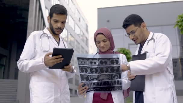 Squadra medica araba che discute all'aperto di fronte alla clinica, guardando tomografia scansione — Video Stock