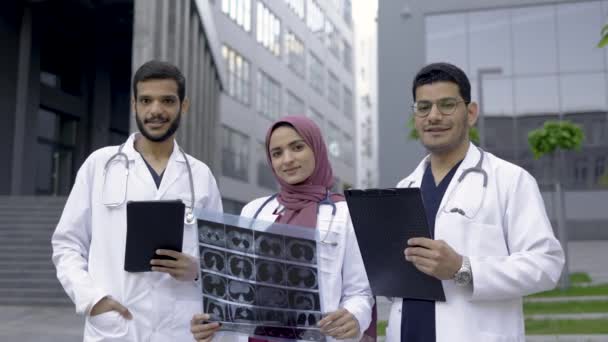 Trzech lekarzy, muzułmanka w hidżabie i dwóch Arabów, pracujących przed kliniką. — Wideo stockowe