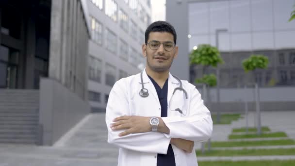 Guapo médico indio al aire libre, vistiendo bata médica y bata blanca de laboratorio, posando brazos cruzados — Vídeo de stock