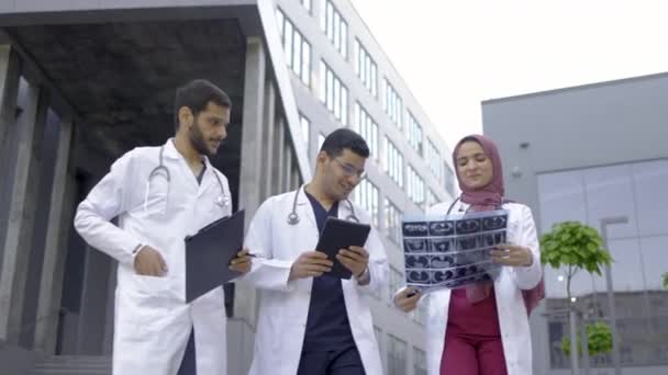 Три лікарі, жінка в хіджабі і двоє чоловіків в медичному одязі, обговорюють пацієнтів рентгенівське КТ-сканування — стокове відео