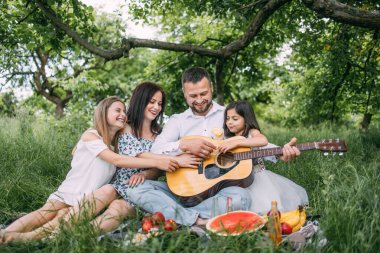 Aile yeşil bahçede gitar şarkılarıyla piknik yapıyor.