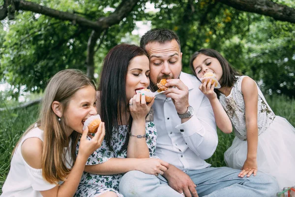 Usmívající se rodiče se dvěma dětmi jíst cupcakes na piknik — Stock fotografie