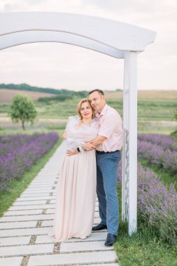 Romantik olgun bir çift, erkek kadına sarılıyor, lavanta tarlasında ahşap kemerin altında duruyor.