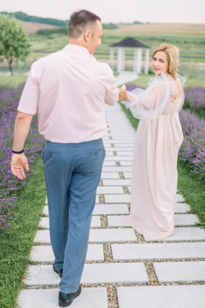 Ξανθιά ώριμη κυρία με κομψό φόρεμα, κρατώντας το χέρι και περπατώντας με τον όμορφο άντρα της έξω — Φωτογραφία Αρχείου