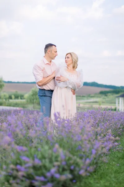 Happy romantic mature couple, posing together looking each other, at beautiful lavender field — Stock Photo, Image