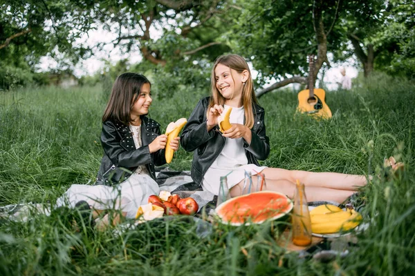 Dos hermanas alegres comiendo plátanos durante el picnic de verano —  Fotos de Stock