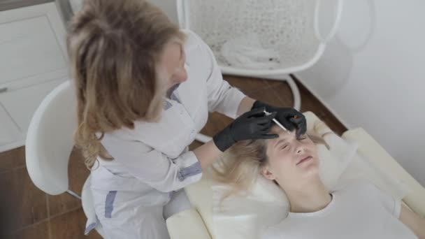 Hände einer Kosmetikerin, die einer schönen Frau Botox zwischen die Augenbrauen spritzt. Korrektur von Mimikfalten im Salon. Verfahren zur Alterung, Verjüngung und Hydratation. — Stockvideo