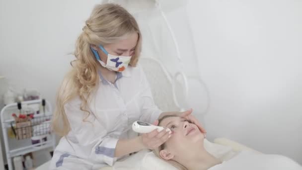 Hardware-Kosmetologie. Junge Ärztin Kosmetikerin entfernt Pigmentflecken, Muttermale, Gefäßsternchen im Gesicht ihrer Klientin mit einem Laser in einer modernen kosmetischen Hautklinik. — Stockvideo