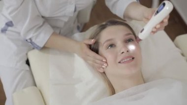 Lazer kozmetolojisi için aletlerle doktorun ellerini kapat ve gülümseyen sarışın kadın için tedavi yap. Benlerin, siğillerin, papillomların, kılcal damarların, pigment damarlarının çıkarılması