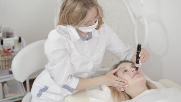 Portrét mladé blond ženy lékař kosmetolog dermatolog pomocí dermatoskopu pro kožní vyšetření obličeje nebo krásné ženy klienta, v nemocnici nebo moderní kosmetické klinice — Stock video