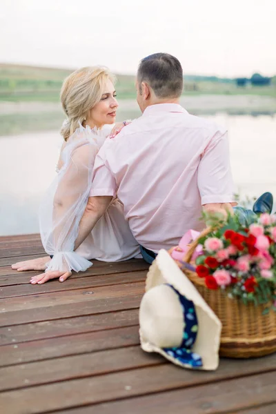 Άντρας και κυρία, κάθονται μαζί στην ξύλινη γέφυρα στην όχθη της λίμνης — Φωτογραφία Αρχείου