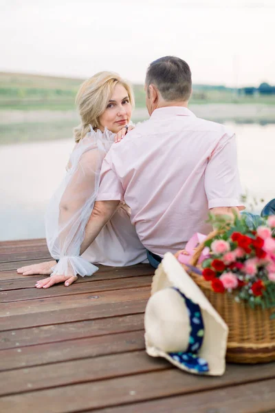 Όμορφος μεσήλικας άντρας και όμορφη γοητευτική κυρία, κάθονται μαζί στην όχθη της λίμνης ή της λίμνης — Φωτογραφία Αρχείου