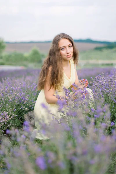 Bela jovem caucasiana de cabelos compridos mulher em um vestido amarelo claro coleta lavanda. — Fotografia de Stock