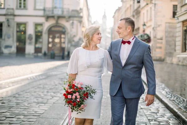 Coppia matura in eleganti vestiti alla moda, passeggiando per la strada della vecchia città europea — Foto Stock