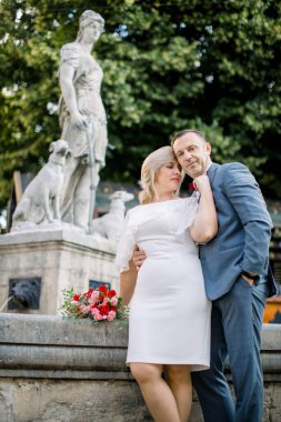 Olgun bir çift şehir çeşmesinin önünde sarılıyor, başka yere bakıyor ve hayal kuruyor.